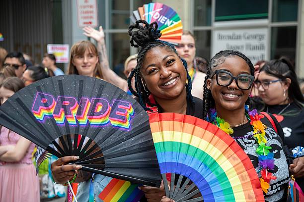 Two smiling people holding Pride fans at a community event