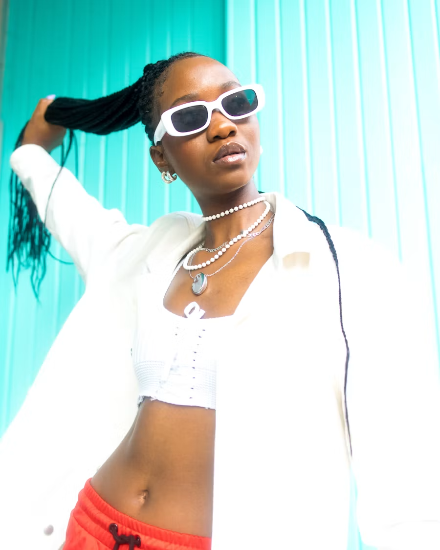 Braided hairstyle, white sunglasses, and layered necklaces against turquoise