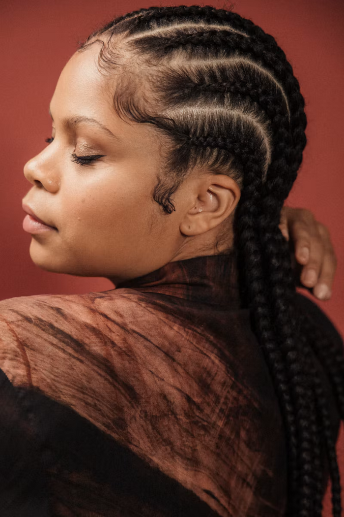 Close-up side portrait with neat dark cornrows against a red background
