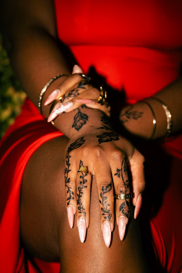 Floral hand tattoos, pink nails and gold jewelry against red fabric