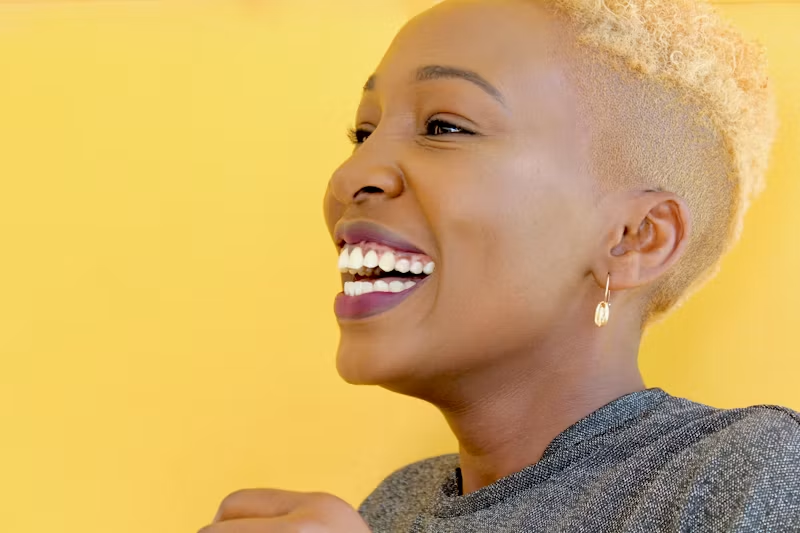 Smiling person with short blonde hair against a yellow background