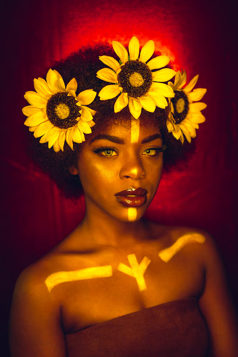 Natural afro crowned with sunflowers, gold makeup and warm red lighting